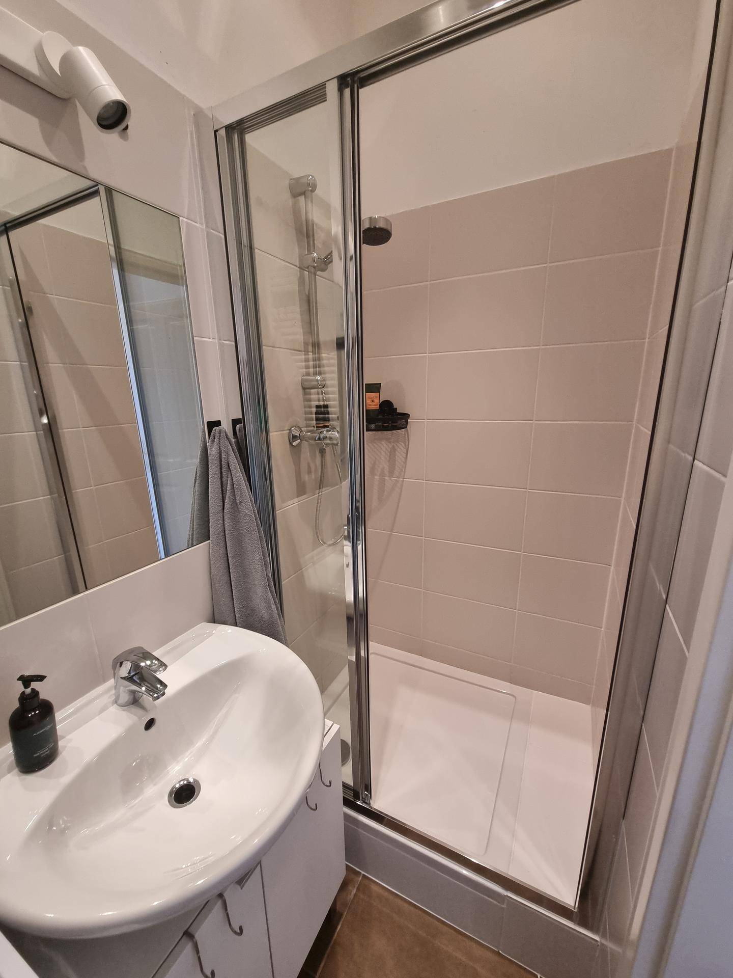 Modernes Badezimmer mit Duschkabine, Waschbecken und Spiegel, hell gefliest.
