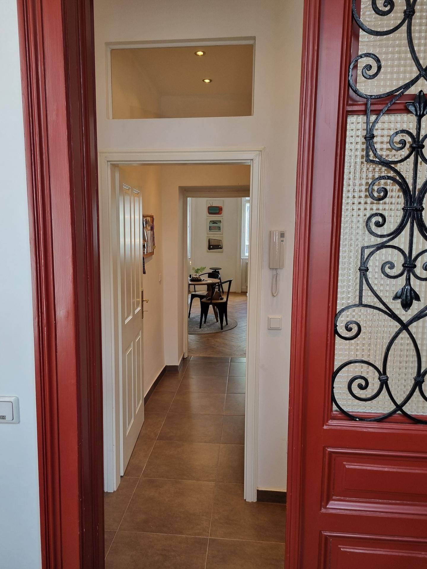 Blick durch die offene Eingangstür mit schmiedeeisernem Detail in den gefliesten Flur der Wohnung.