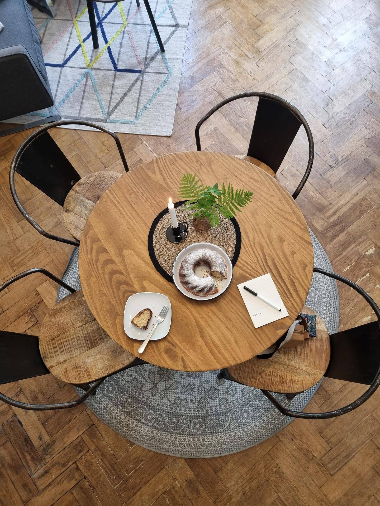 Runder Holztisch mit Stühlen und Kuchen, auf einem Teppich im Essbereich mit Fischgrätparkett.