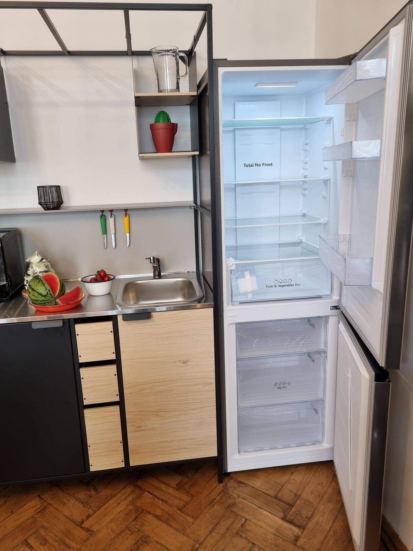Kompakte Küchenzeile mit Spüle, offenen Regalen und einem geöffneten Kühlschrank.