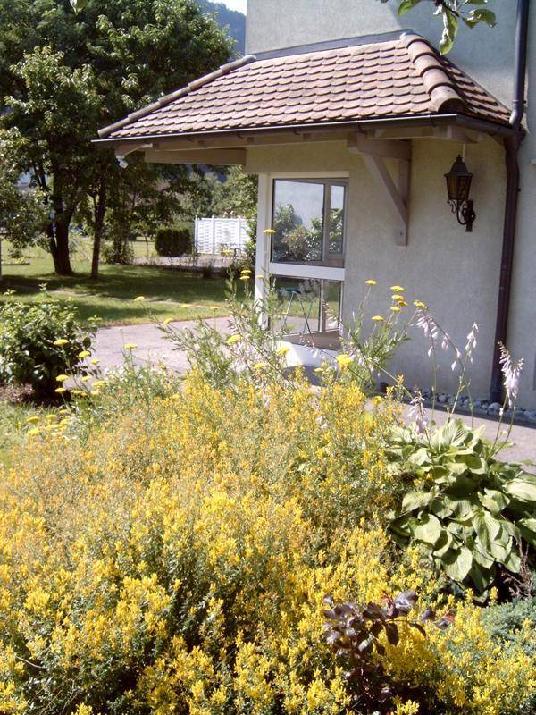 Blühender Gartenbereich vor einem überdachten Eingang mit Ziegeldach.