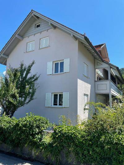 Seitenansicht des Mehrfamilienhauses mit Balkonen und gepflegter Hecke im Vordergrund.