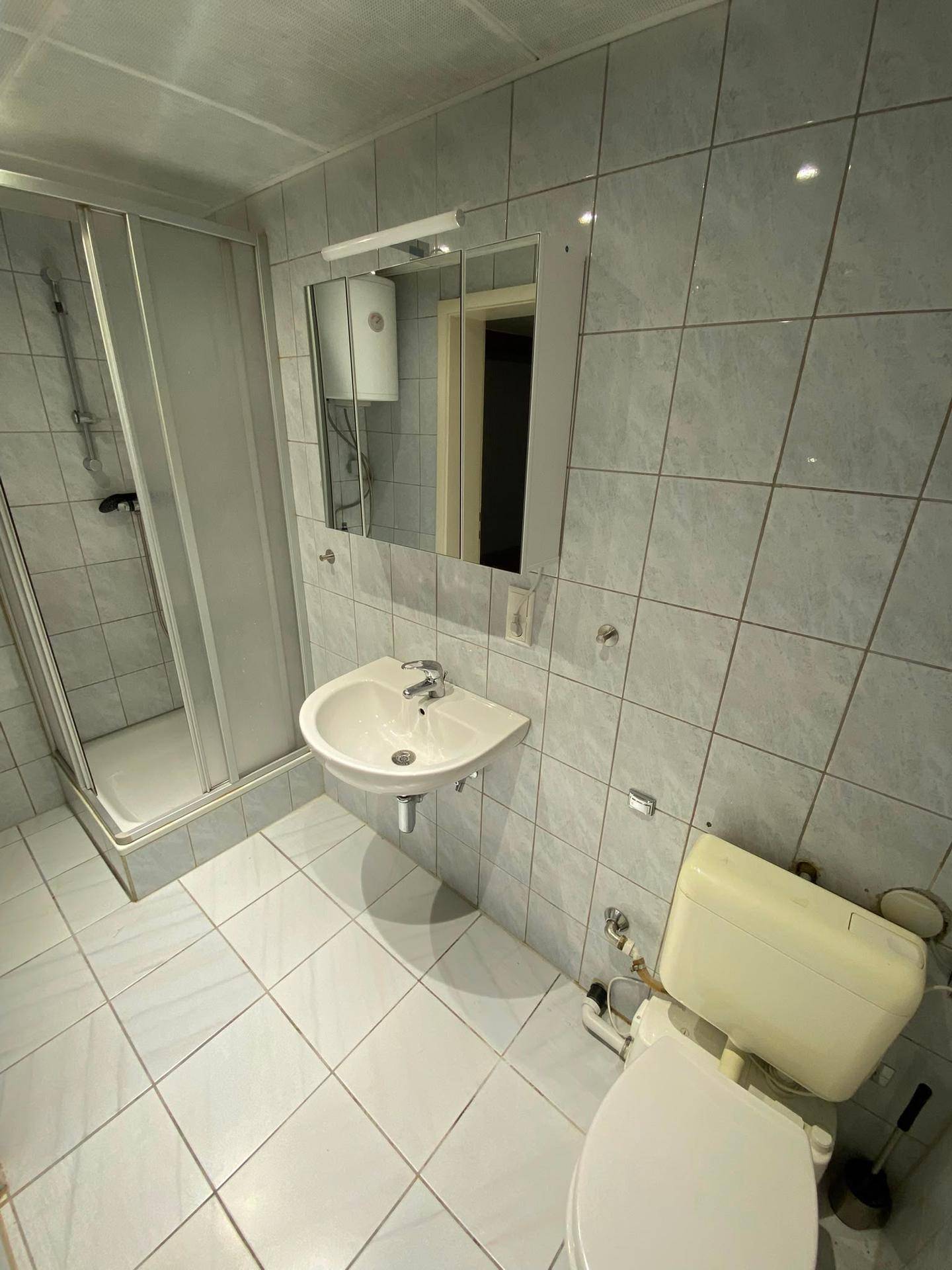 Funktionales Badezimmer mit Duschkabine, Waschbecken und WC in hellen Fliesen.