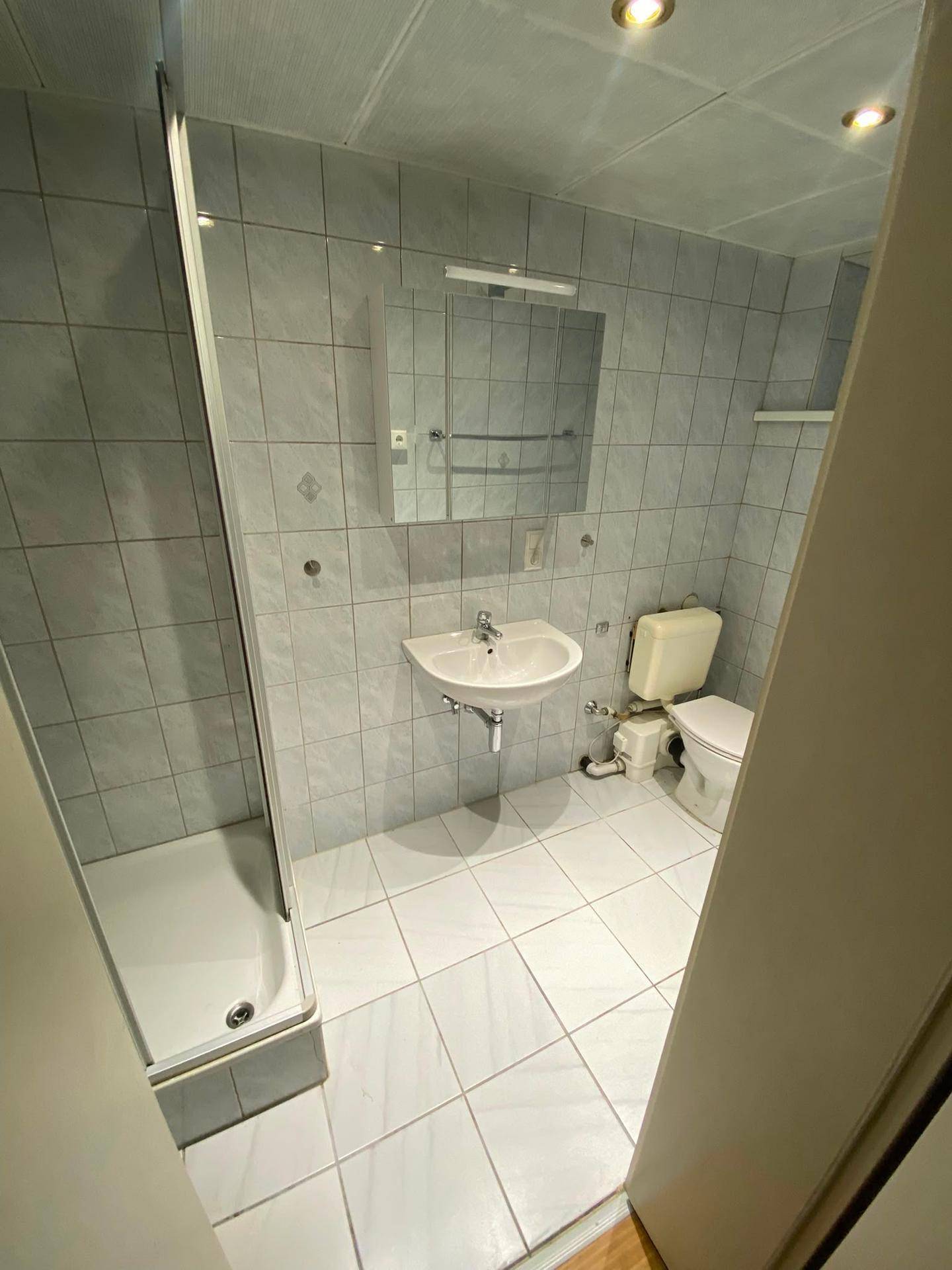 Badezimmer mit hellblauen Fliesen, Waschbecken, Toilette und Duschkabine.