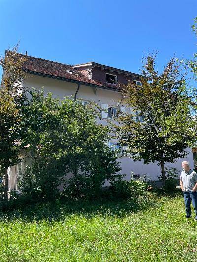 Rückansicht des Hauses mit Gartenfläche und Bäumen unter blauem Himmel.