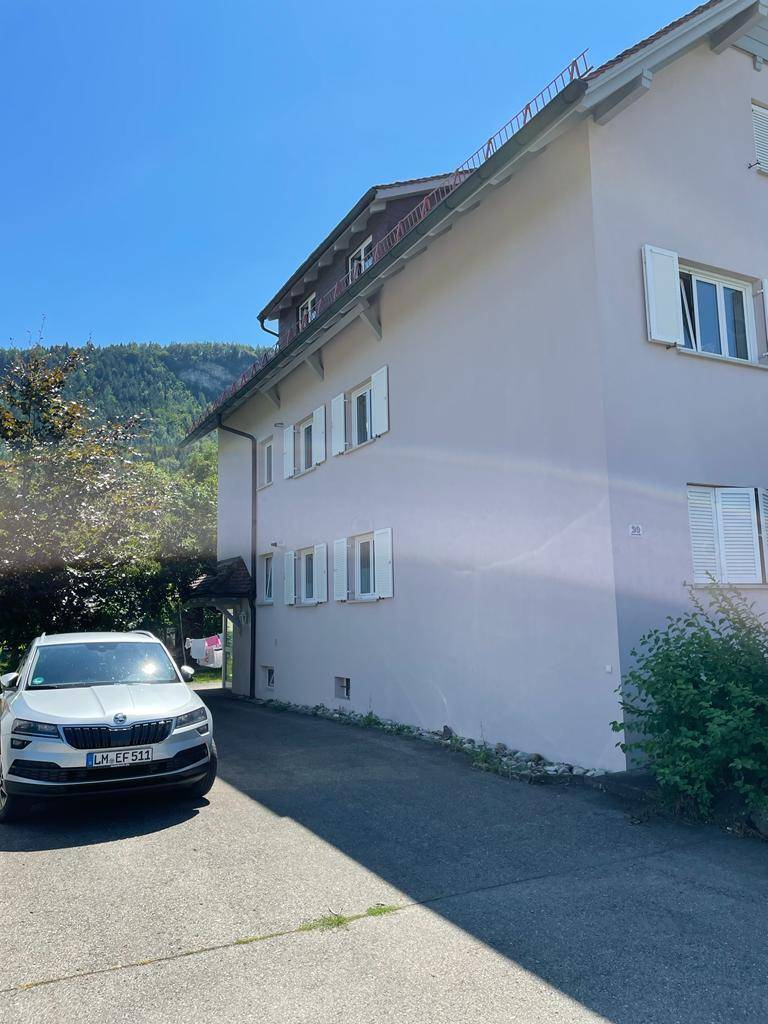 Vorderansicht des Hauses mit geparktem Auto und Blick auf die umliegenden Berge.