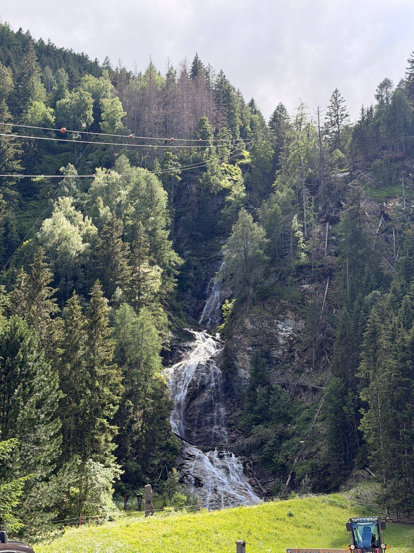 Beeindruckender Wasserfall inmitten eines dichten Bergwaldes unter hellem Himmel.