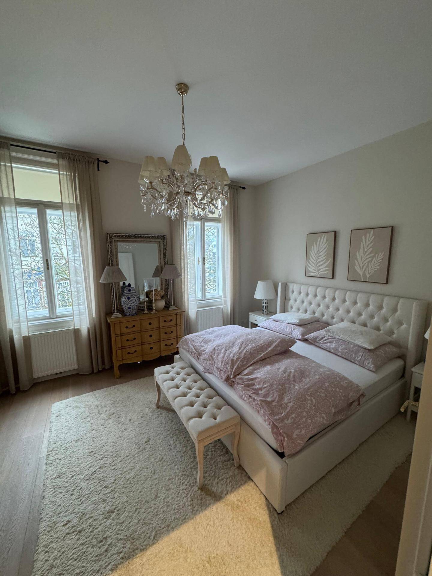 Gemütliches Schlafzimmer mit großem Bett, Kronleuchter und viel natürlichem Licht.