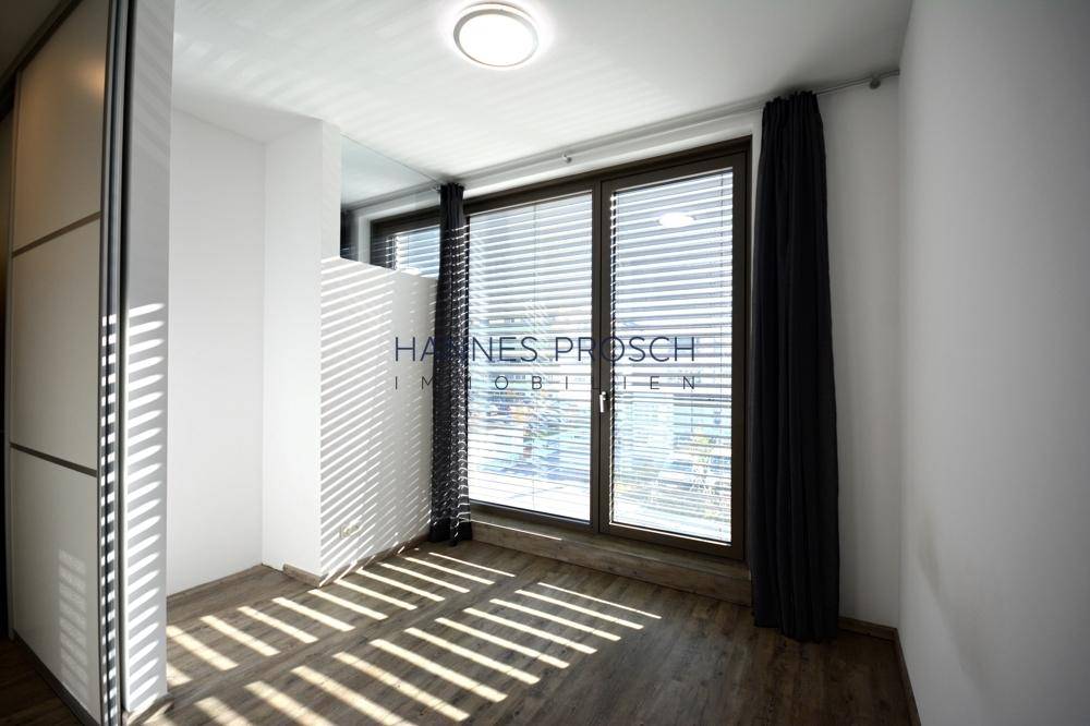 Heller Raum mit großen Fenstern, Jalousien und integriertem Kleiderschrank.