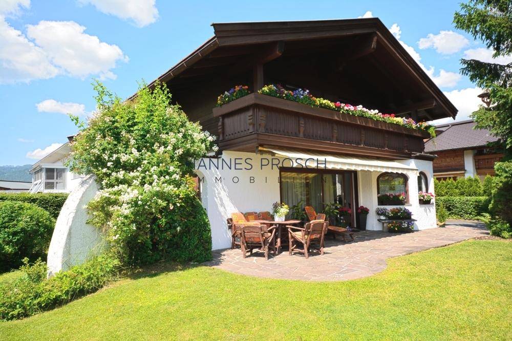 Charmantes Haus mit blühenden Pflanzen, Balkon und einer einladenden Terrasse mit Gartenmöbeln.