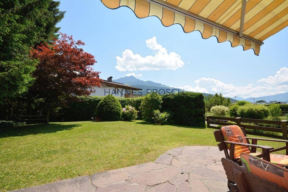 Großer, gepflegter Garten mit Steinterrasse, Markise und weitem Blick auf die umliegende Berglandschaft.