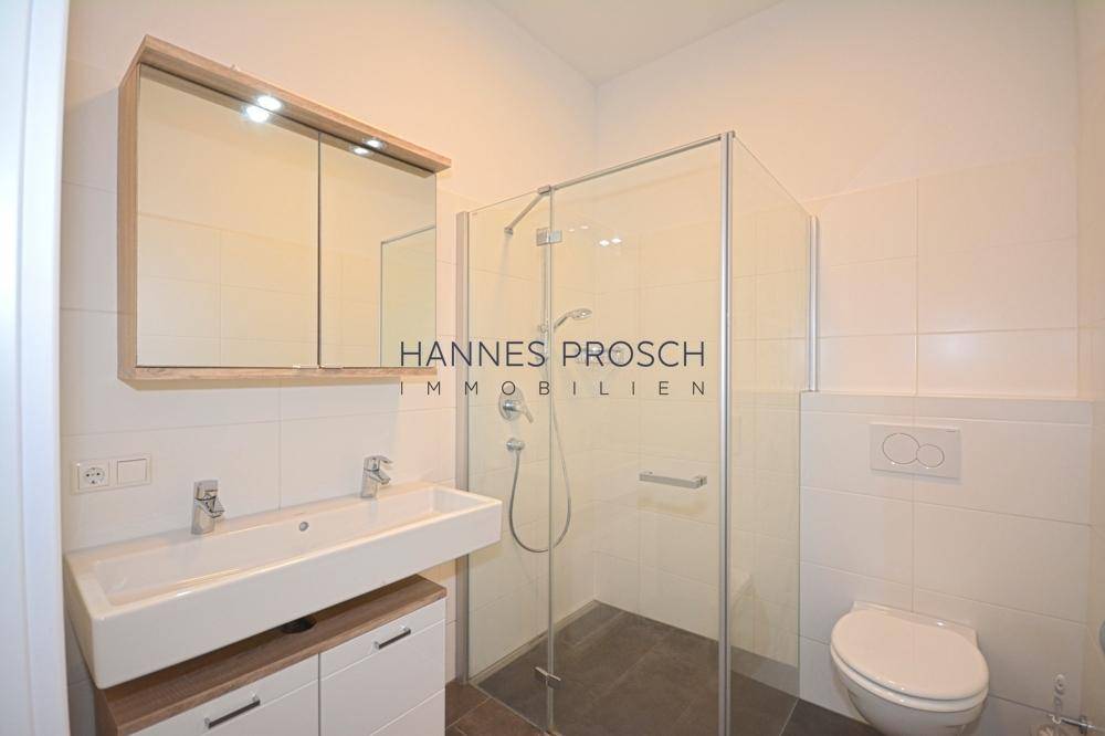 Helles Badezimmer mit moderner Duschkabine, wandhängendem WC und Spiegelschrank.