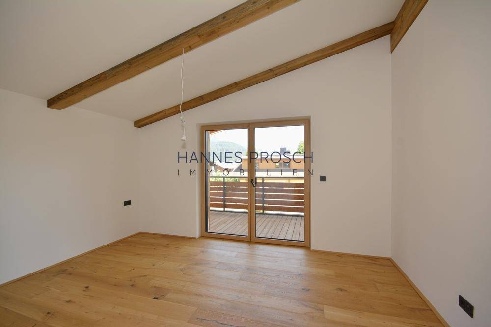 Helles Schlafzimmer mit Holzboden, sichtbaren Holzbalken und direktem Zugang zum Balkon.