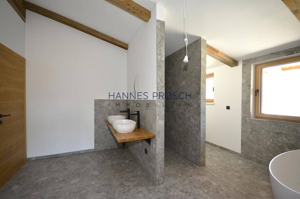 Modernes Badezimmer im Bau mit Doppelwaschbecken, grauen Fliesen und sichtbaren Holzbalken.