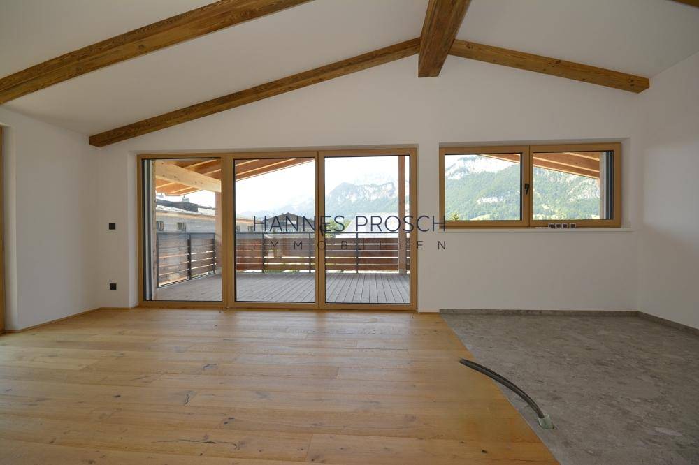 Heller Wohnraum mit Holzbalken, Holzboden und großen Schiebetüren zum Balkon mit Bergblick.