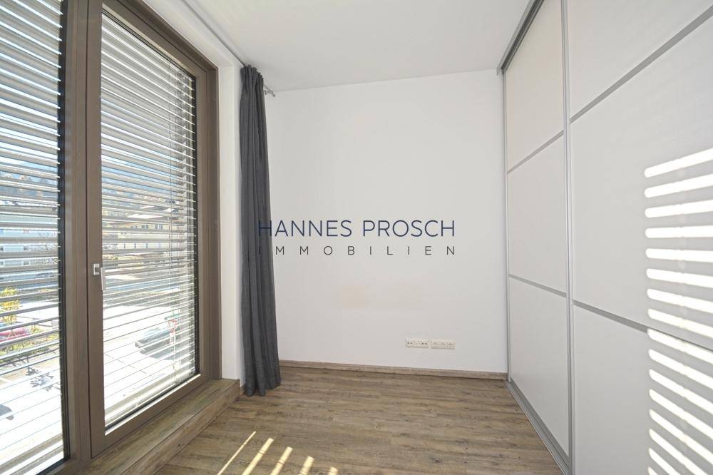 Lichtdurchfluteter Raum mit großem Fenster, Jalousien und weißem Einbauschrank.
