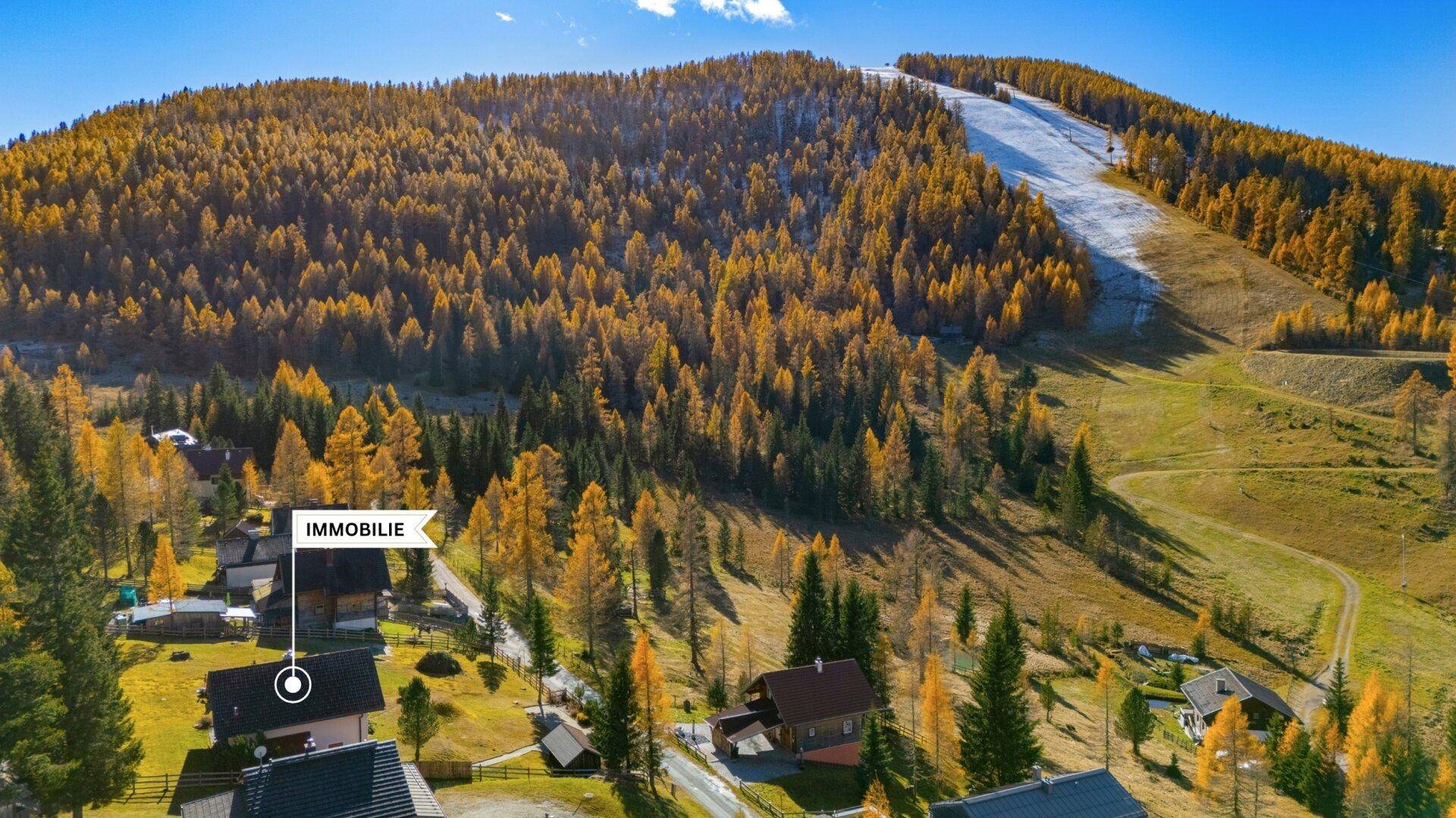 Luftaufnahme der Immobilie in einer bergigen Waldlandschaft mit Skipiste im Herbst.