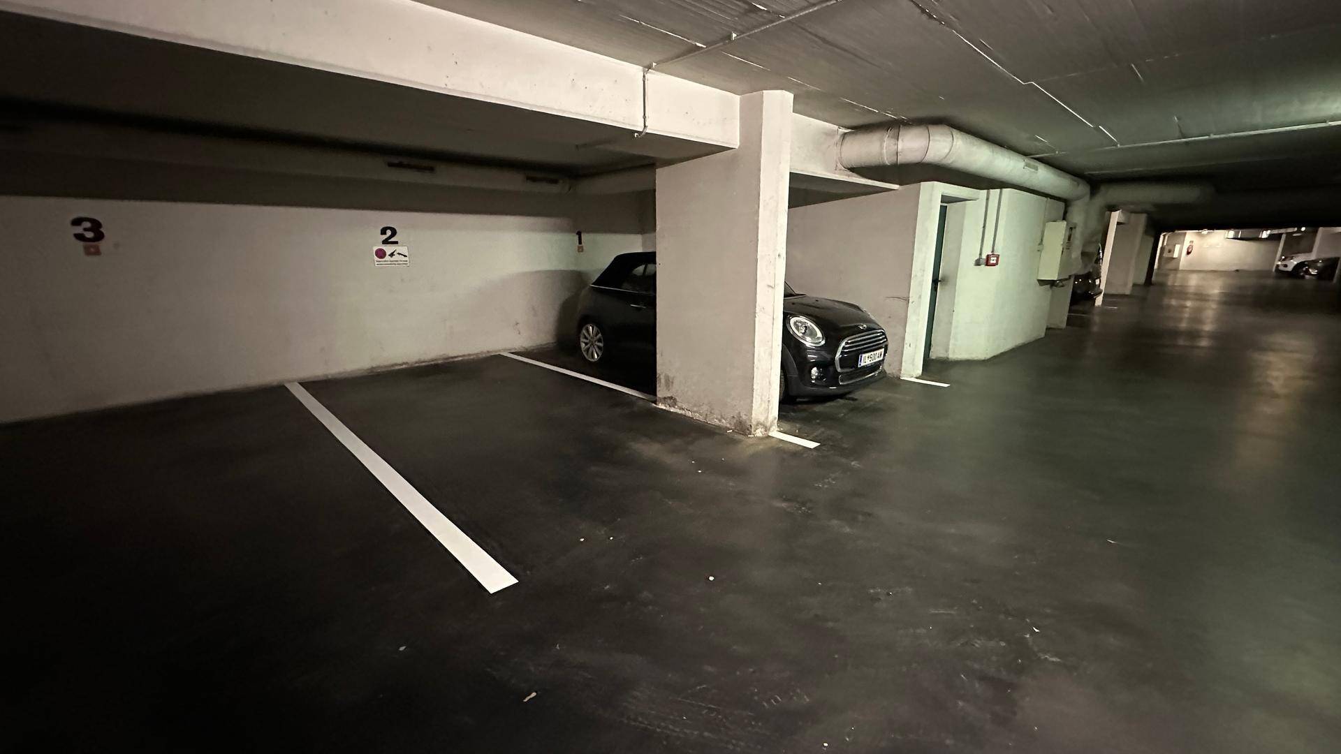 Geräumige Tiefgarage mit einem geparkten schwarzen Mini Cooper und markierten Stellplätzen.