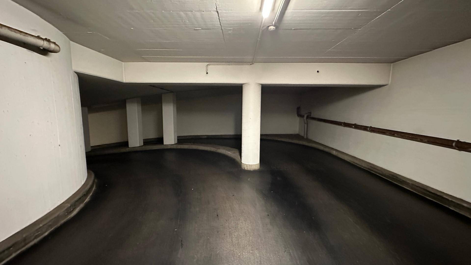 Geschwungene Rampe in einer Tiefgarage mit weißen Wänden und Betonstützen.