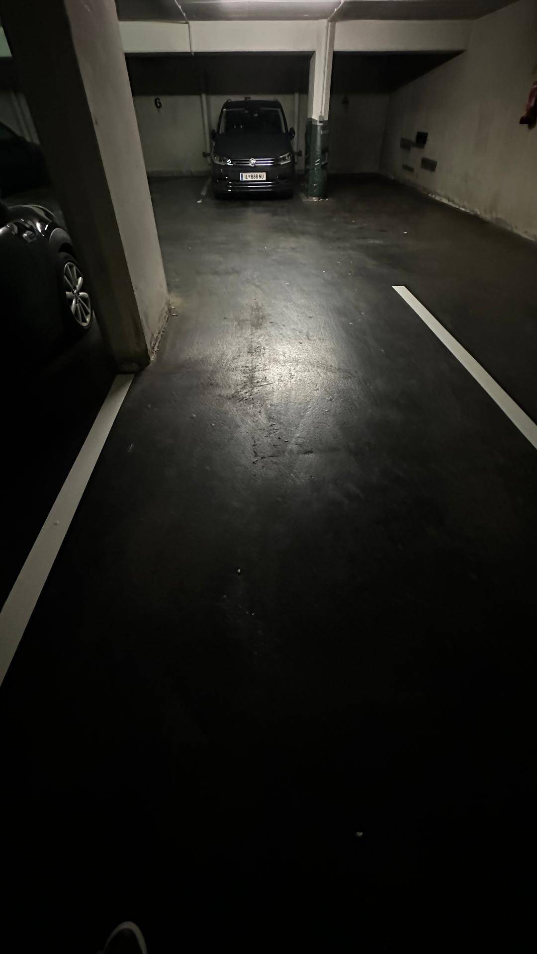 Langer Gang in einer dunklen Tiefgarage mit einem geparkten Fahrzeug am Ende des Ganges.
