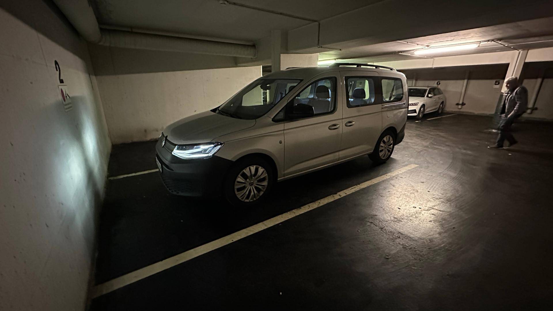 Silberner Van auf einem markierten Stellplatz in einer Tiefgarage mit Betonwänden.