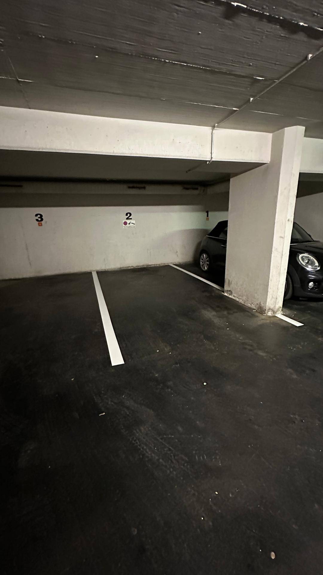 Detailansicht eines Parkplatzes in der Tiefgarage mit einem teilweise sichtbaren schwarzen Mini Cooper.