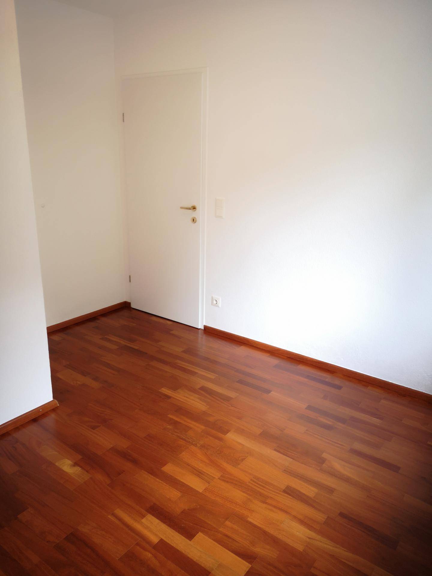 Leeres Zimmer mit dunklem Holzboden und weißer Tür, bereit zur individuellen Gestaltung.