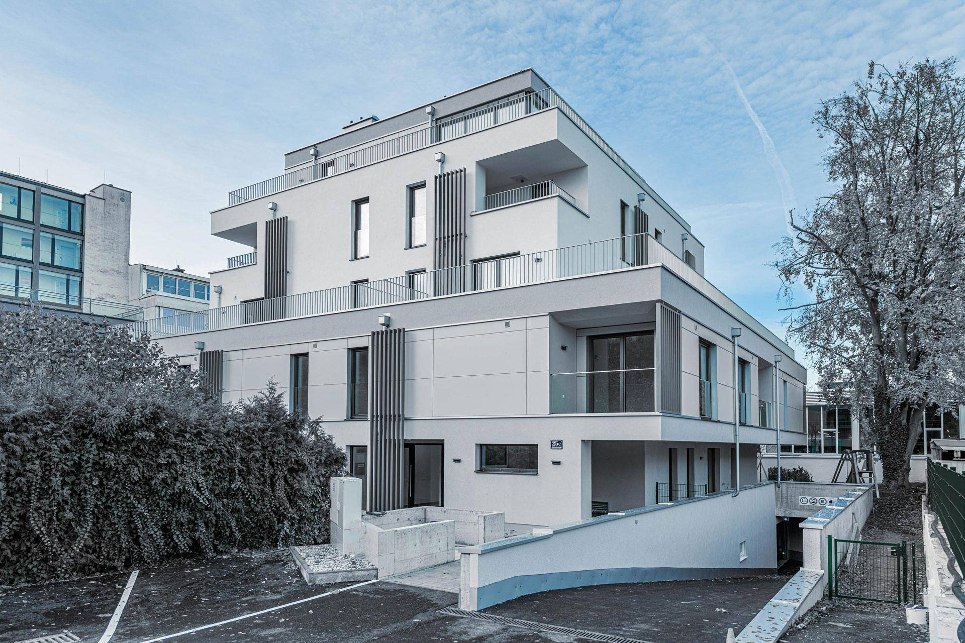 Moderne Wohnanlage mit Tiefgaragenzufahrt, umgeben von gepflegten Grünflächen und Bäumen.