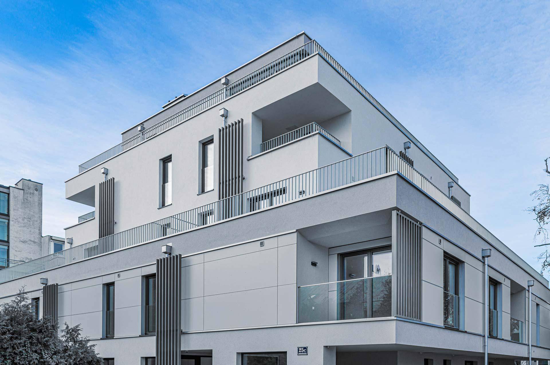 Detailansicht der modernen Fassade mit gestuften Balkonen und großen Fensterfronten unter blauem Himmel.