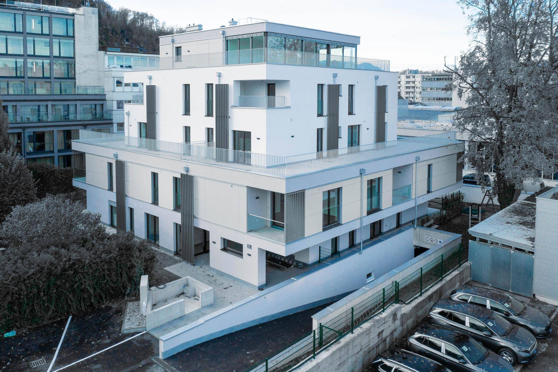 Zeitgenössisches Wohngebäude mit weißer Fassade, Balkonen und einer Tiefgaragenzufahrt.