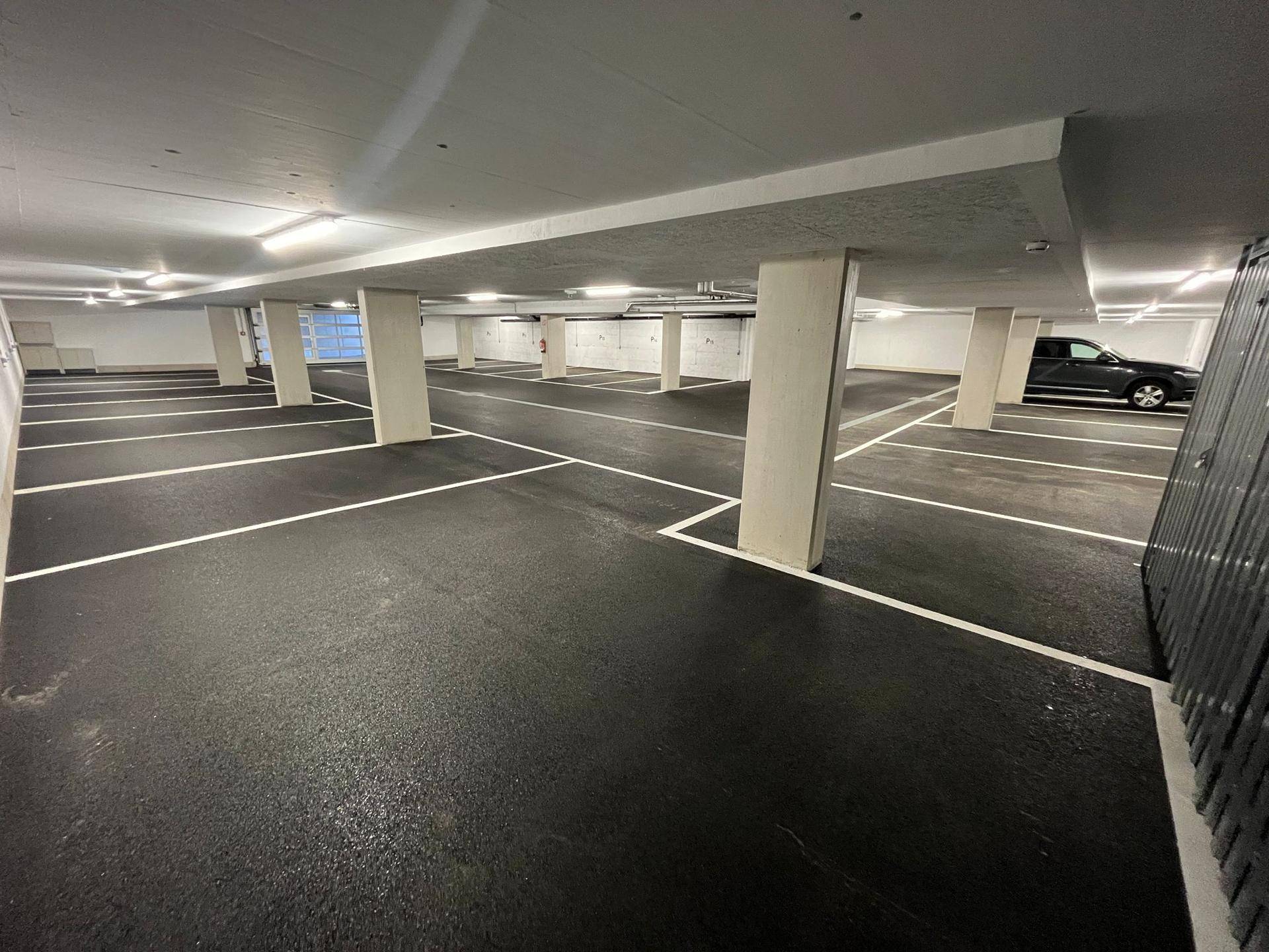 Geräumige und gut beleuchtete Tiefgarage mit vielen markierten Stellplätzen und Säulen.