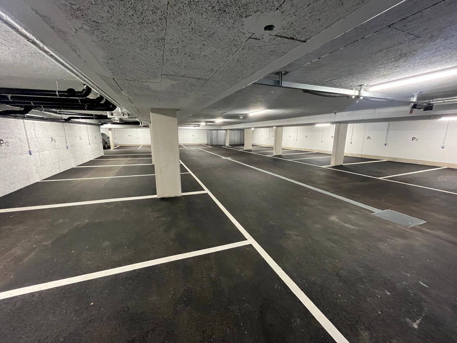 Geräumige und gut beleuchtete Tiefgarage mit vielen Stellplätzen und klaren Markierungen.