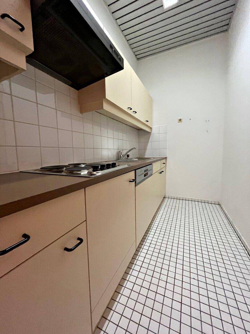 Kleine Küche mit beigen Schränken, weißem Fliesenspiegel, Kochfeld, Spüle und Geschirrspüler.
