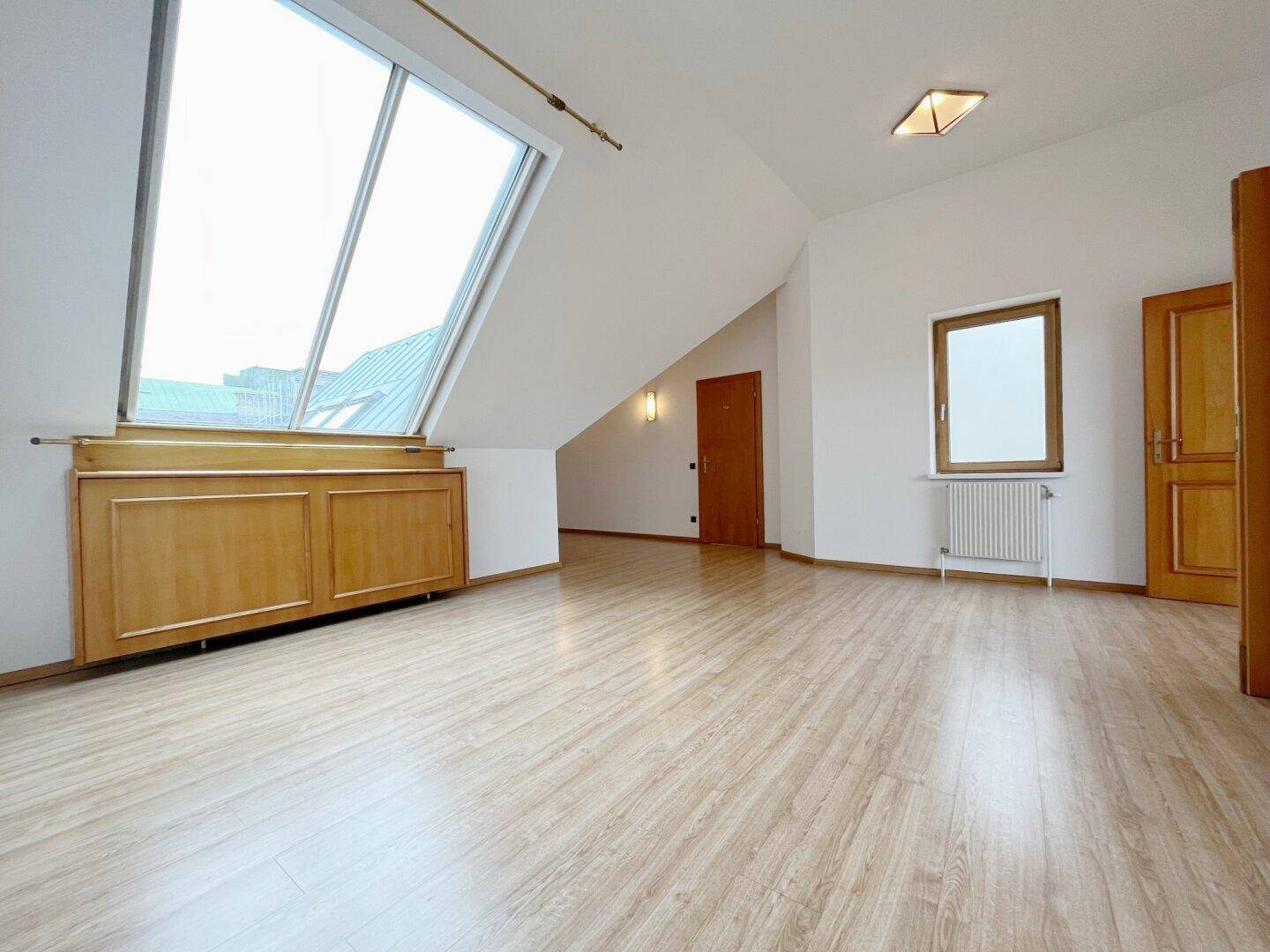 Leerer Raum mit Laminatboden, Holztür, großem Dachfenster und Heizkörper.