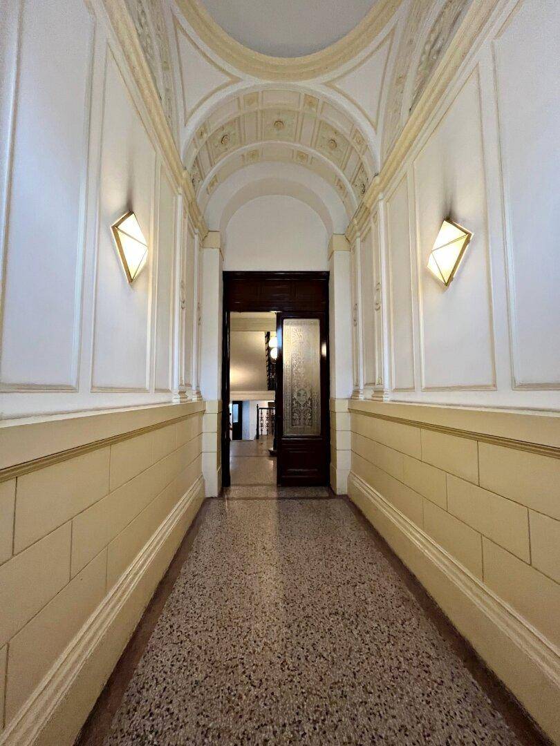 Historischer Flur mit Gewölbedecke, Stuckverzierungen, Wandleuchten und Terrazzoboden.