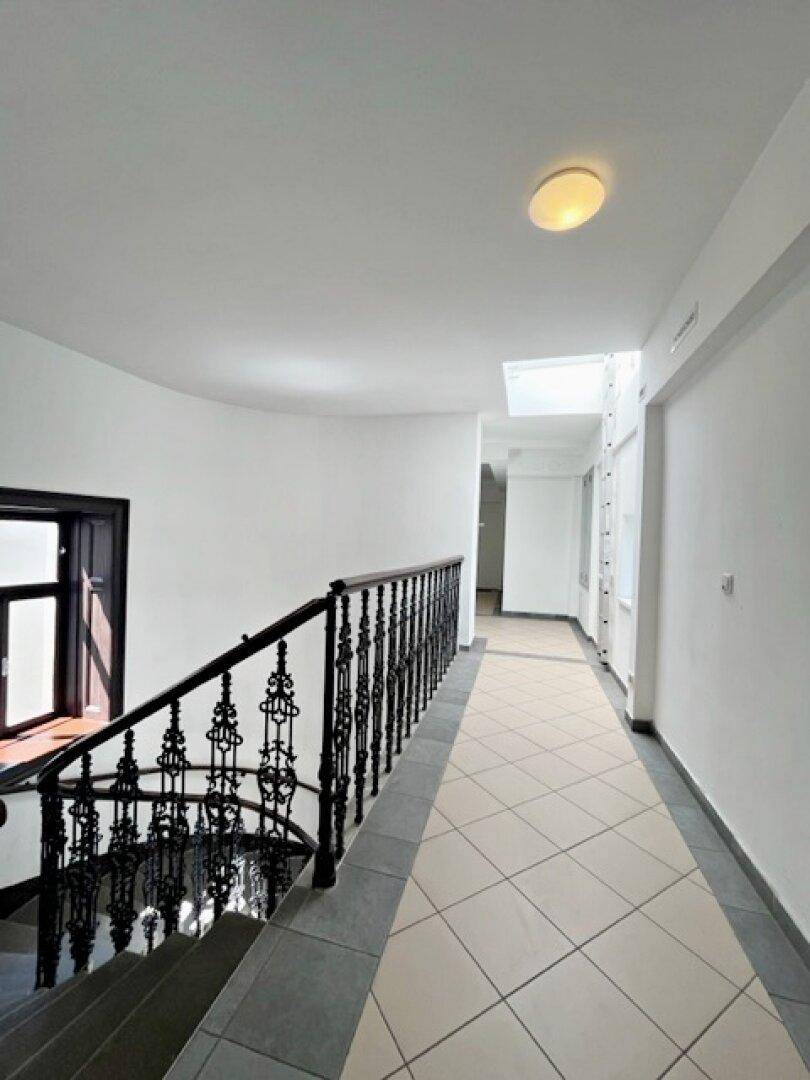 Heller Treppenaufgang mit schmiedeeisernem Geländer und Fliesenboden in einem Altbau.