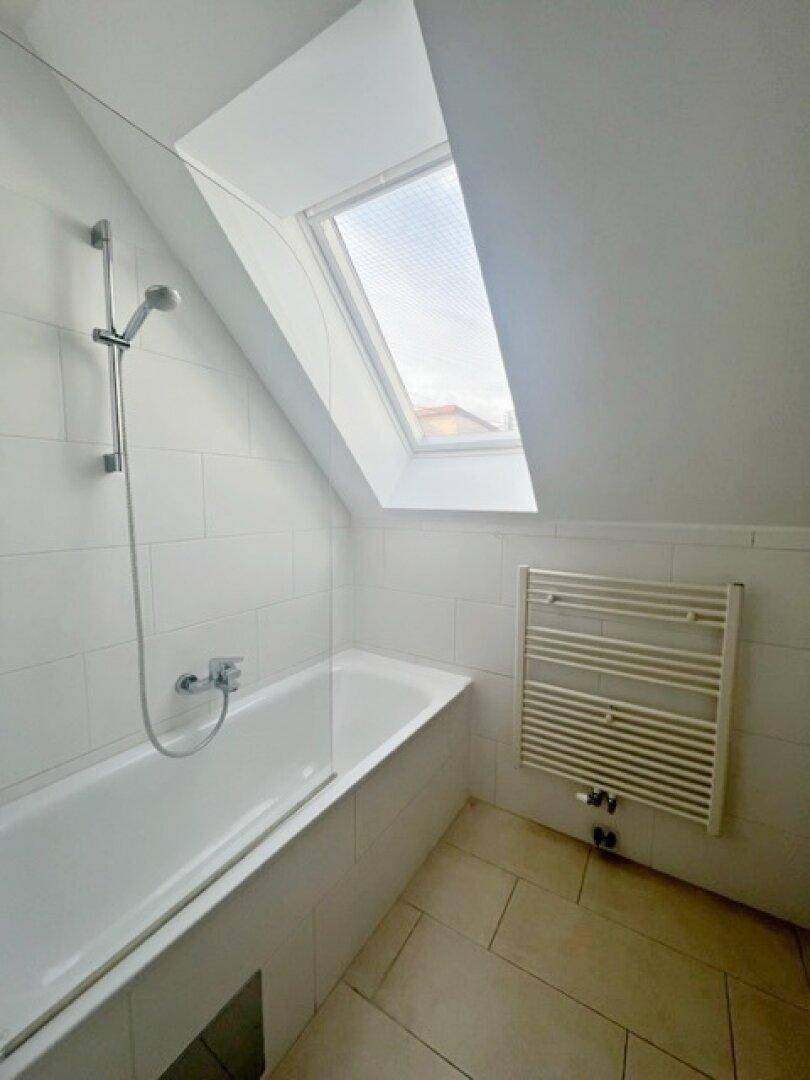 Modernes Badezimmer mit Badewanne, weißen Fliesen, Dachschräge und einem Dachfenster für Tageslicht.