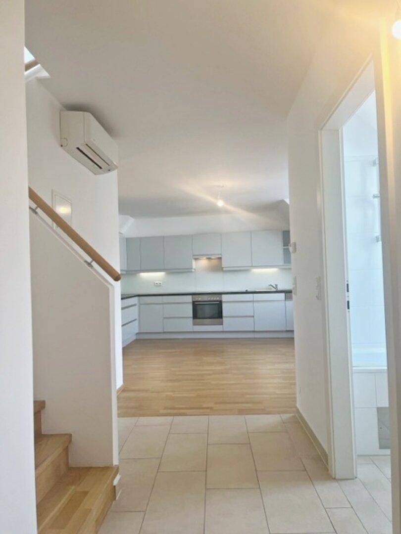 Flur mit Fliesenboden und Treppe, der zu einer modernen Küche im Hintergrund führt.