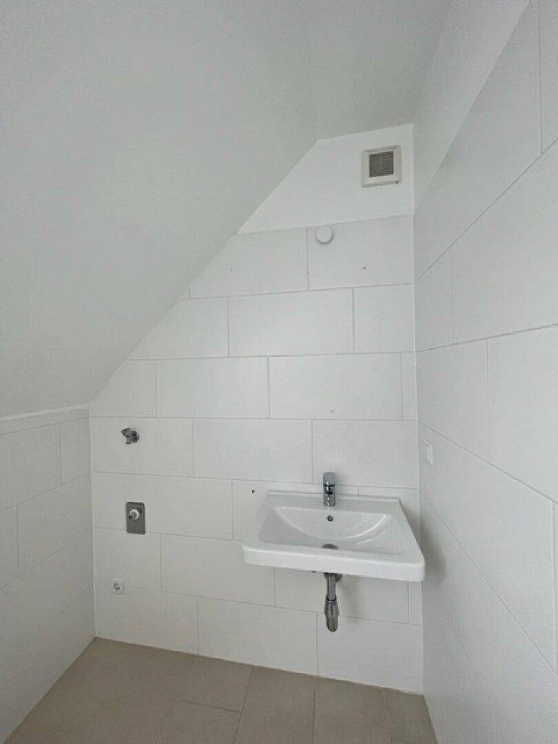 Kleiner, heller Raum mit weißen Fliesen, Waschbecken und Dachschräge, ideal als Gäste-WC.