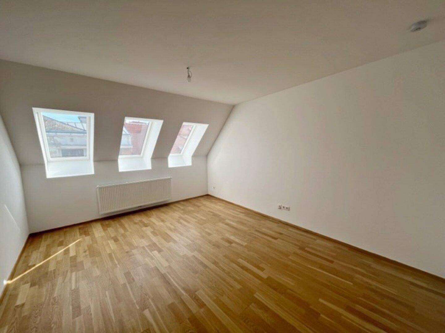 Heller Raum im Dachgeschoss mit Holzparkettboden und drei Dachfenstern, die viel Tageslicht hereinlassen.