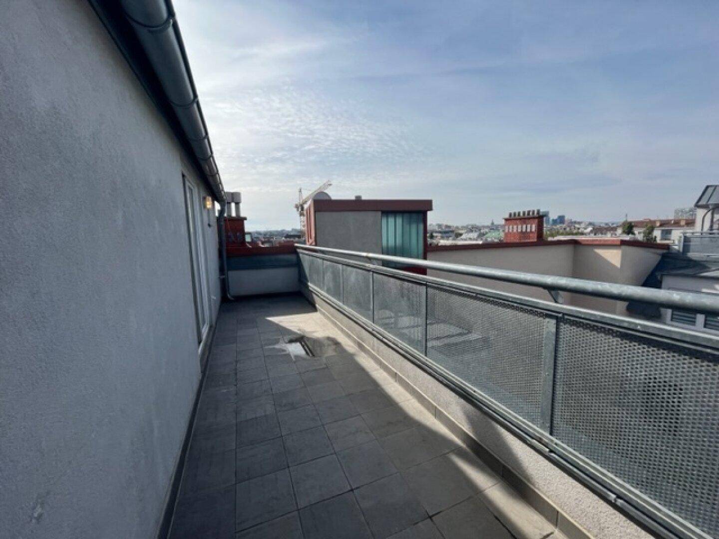 Geräumige Dachterrasse mit Fliesenboden und Metallgeländer, ideal für Entspannung im Freien.