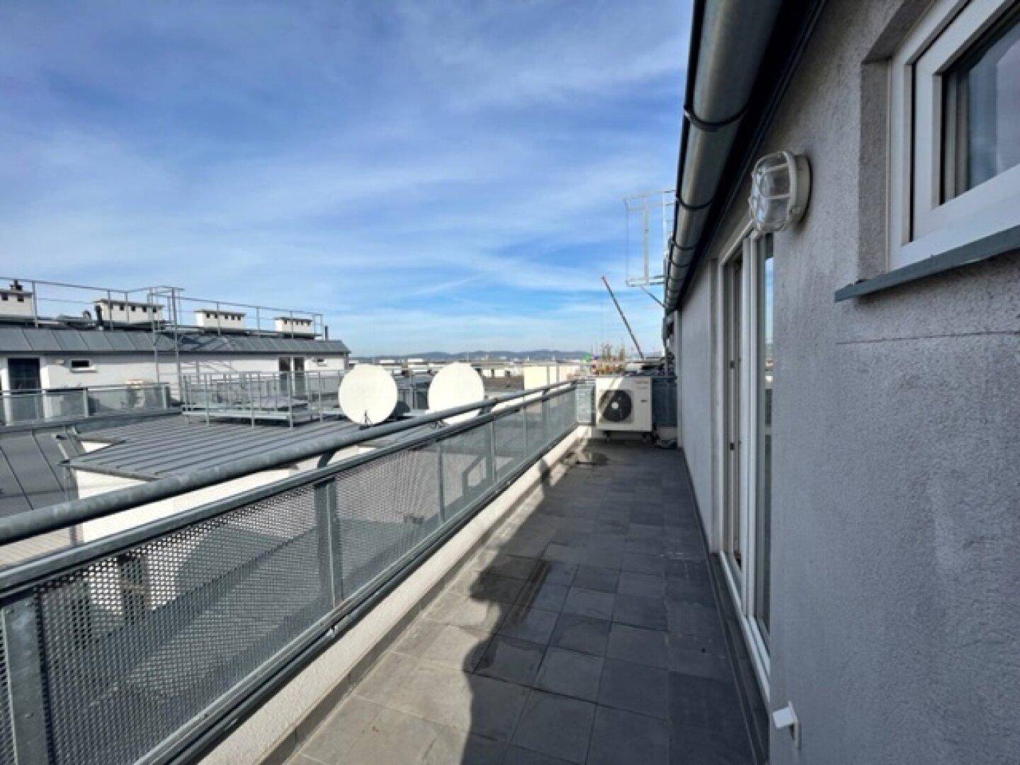Lange Dachterrasse mit Fliesenboden und Metallgeländer, bietet einen weiten Blick über die Stadt.