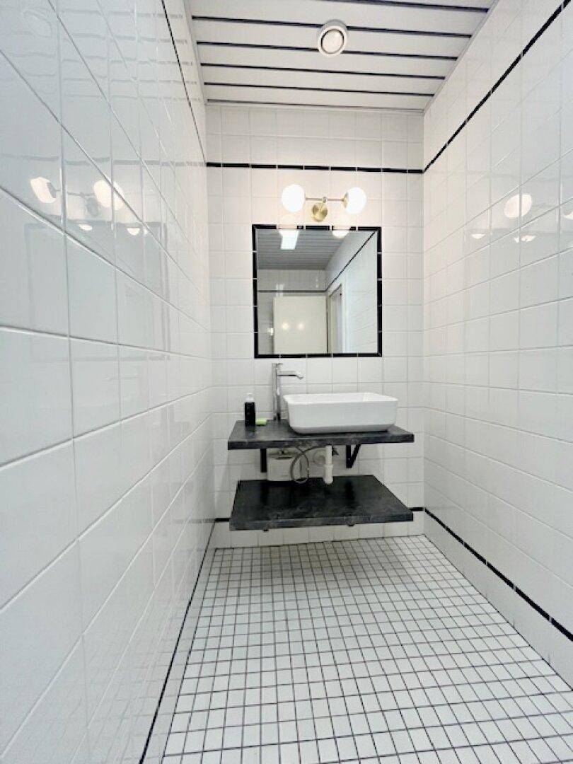 Modernes Badezimmer mit weißen Fliesen, schwarzem Akzent und schwebendem Waschtisch mit Aufsatzbecken.