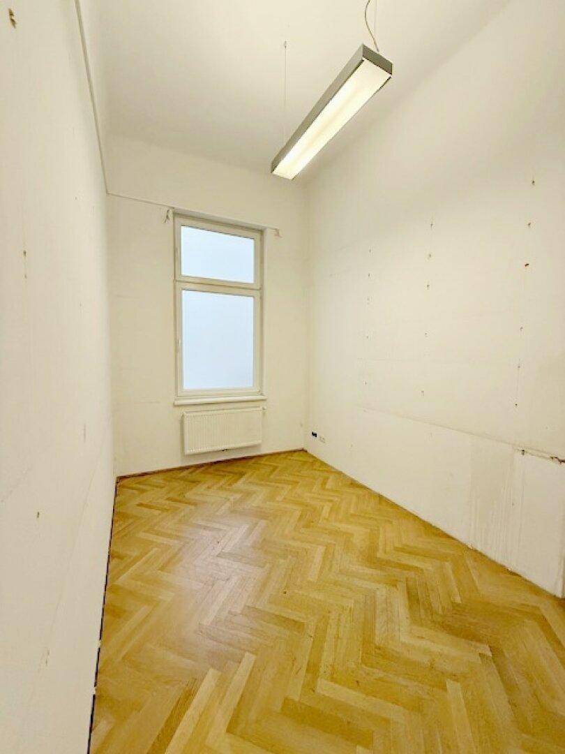 Kleiner, heller Raum mit Fischgrätparkett und einem Fenster, geeignet als Büro oder Abstellraum.