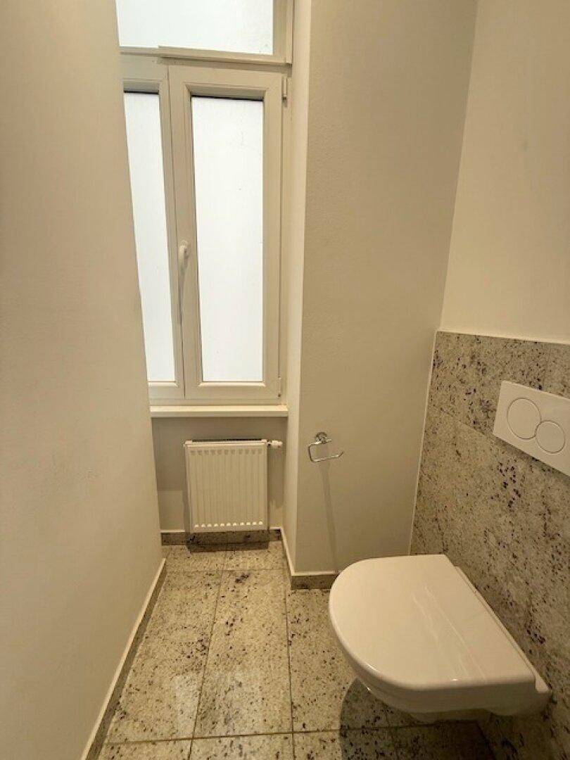 Modernes Gäste-WC mit Fenster, Wand-WC und Granitfliesen, in gutem Zustand.