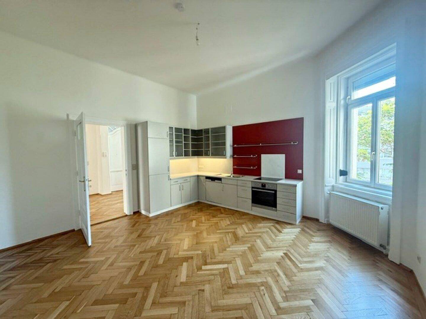 Moderne Einbauküche mit grauen Schränken, roter Rückwand und integrierten Geräten in hellem Raum.