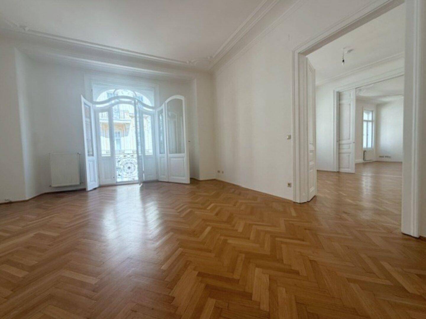 Elegantes Wohnzimmer mit Fischgrätparkett und einem französischen Balkon mit schmiedeeisernem Geländer.