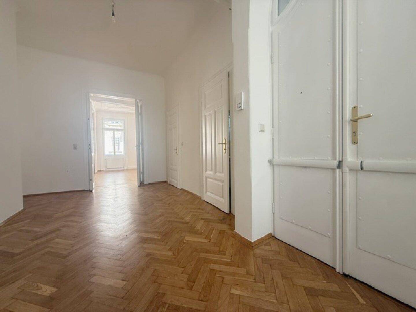 Heller Eingangsbereich mit Fischgrätparkett und einer großen Doppeltür, die den Zugang zur Wohnung bildet.