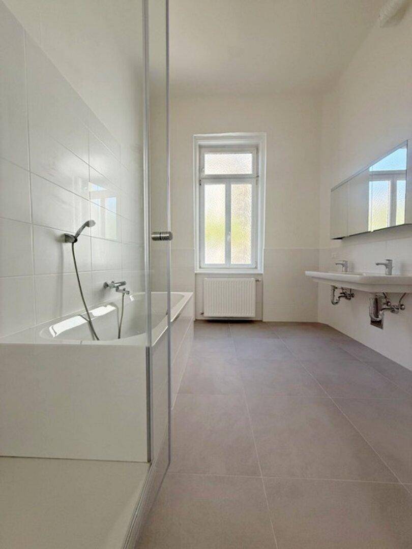 Modernes Badezimmer mit Badewanne, Duschabtrennung, zwei Waschbecken und einem Fenster.