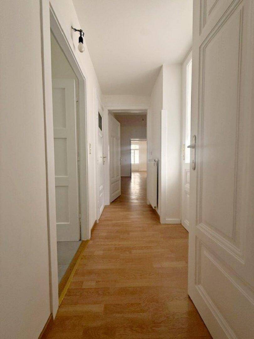 Langer Flur mit hellem Holzboden und weißen Wänden, der zu den verschiedenen Zimmern führt.
